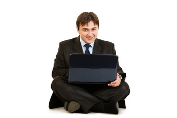Smiling businessman sitting on floor and working on laptop