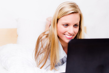 junge frau liegt mit laptop im bett
