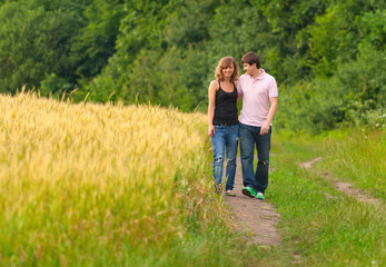 Naklejka na ściany i meble Young couple walking on the road in a field of wheat