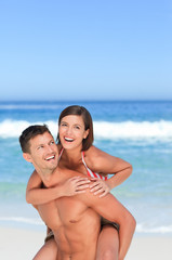 Fototapeta premium Handsome man having wife a piggyback on the beach