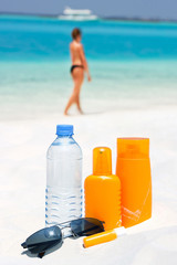 Sunglasses, water and sun protection cream on beach background