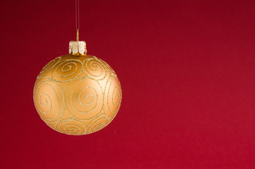 Goldene Weihnachtsbaumkugel vor rotem Hintergrund