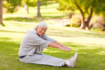 Naklejka na ściany i meble Retired woman doing her stretches in the park