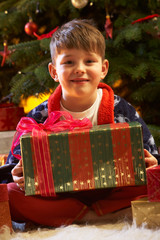 Obraz na płótnie Canvas Young Boy Opening Christmas Present In Front Of Tree