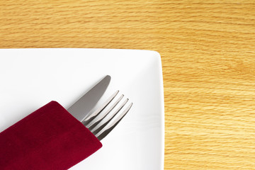 Knife and fork in red napkin on plate