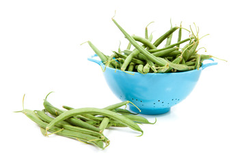 blue colander with long green beans over white background