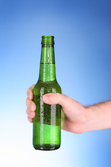 Bottle of beer in hand on blue background