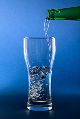 pouring clean water in glass on blue background