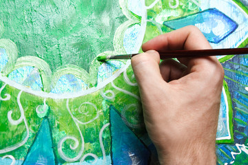closeup of man painting green picture with circle pattern, manda