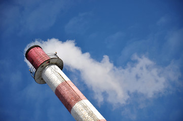 Factory chimney with white smoke scraping sky