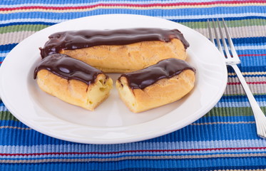 Two Chocolate Covered Eclairs on White Plate and Placemat