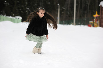 Fototapeta na wymiar Adorable little girl in green tutu dances outside in snow