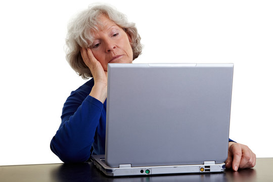 Seniorin schaut gelangweiligt auf Laptop