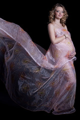 Beautiful blonde pregnant woman in silk dress in studio