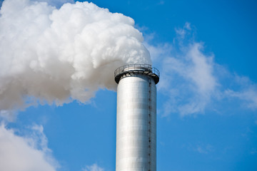 qualmender Schornstein mit weißem Rauch, blauer Himmel