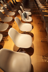 several rows of white plastic chairs; brochure standing on chair