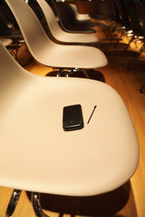 several rows of plastic chairs; smartphone with stylus on chair