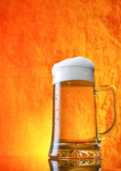 Glass of beer close-up with froth over orange background