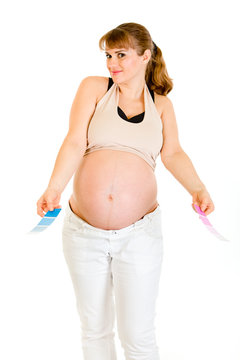 Confused pregnant woman holding color paint samples