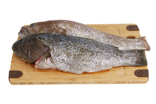 Two scaled grouper fish on bamboo cutting board isolated