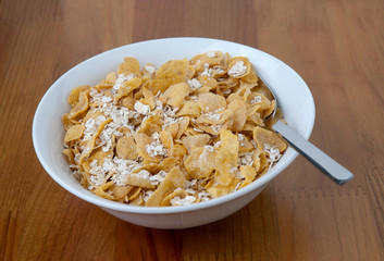 White bowl with a spoon, corn and oats flakes on wooden table.