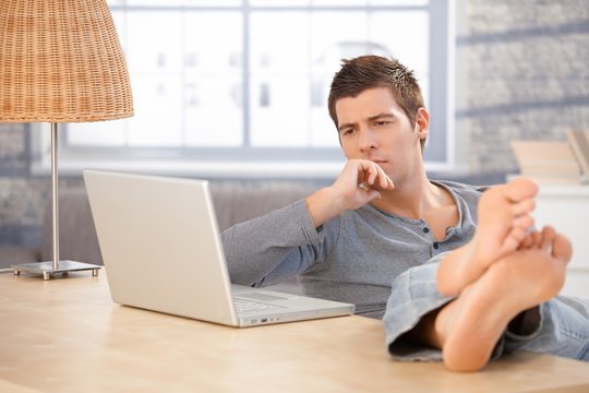 Young man thinking looking at laptop