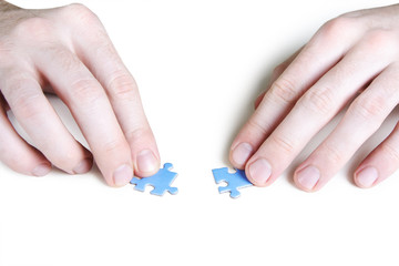 closeup of mans hands assembling two blue puzzle pieces, isolate