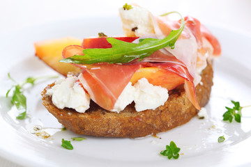 Sandwich with ham, fresh peach and soft goat cheese on white pla