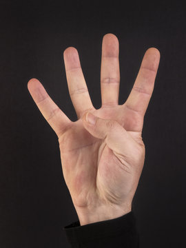 Mano de hombre formando el número cuatro con la mano sobre un fondo negro. Vista de frente y de cerca