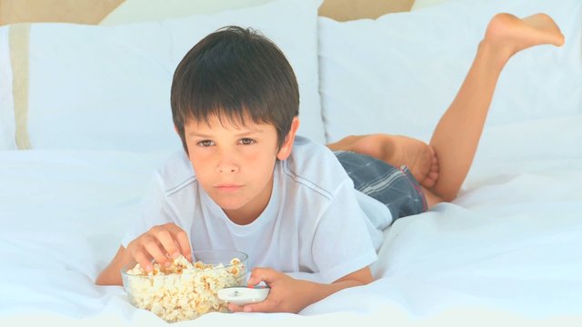 A little boy eating popcorn in front of the tv