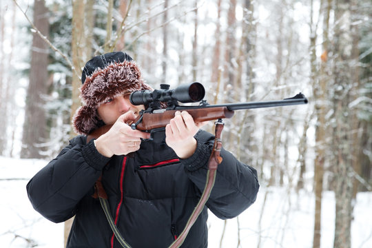 Hunter in a fur cap with ear flaps with sniper rifle in winter f