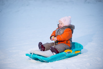 Adorable baby sliding on sleigh from hill in park and smile