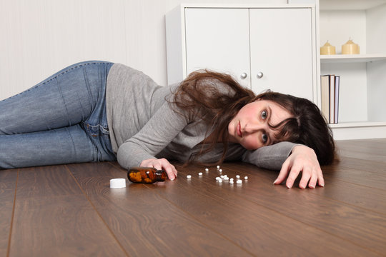 Depressed teenage girl lying on floor with pills
