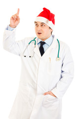 Surprised doctor in Santa hat with rised finger. Idea gesture.