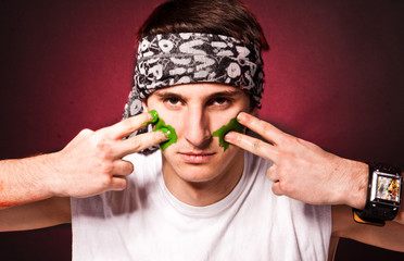 Young caucasian man drawing strips on face with green paint