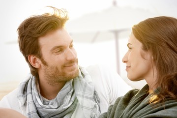 Young couple sitting on summer beach smiling