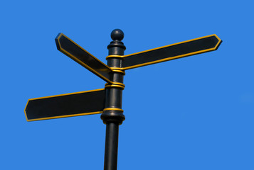 Black and gold painted metal sign post against a blue sky