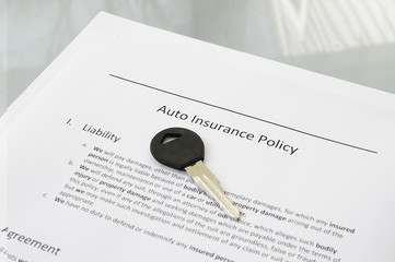 Closeup of a car key and auto insurance policy