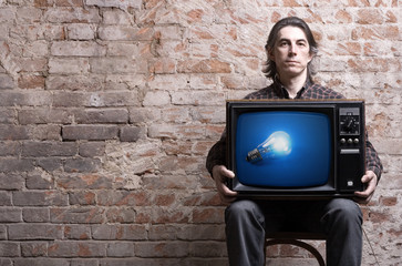 A man holding a retro TV with glowing light bulb .