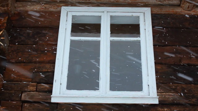 Slow motion of snowing against the window of an old wooden house