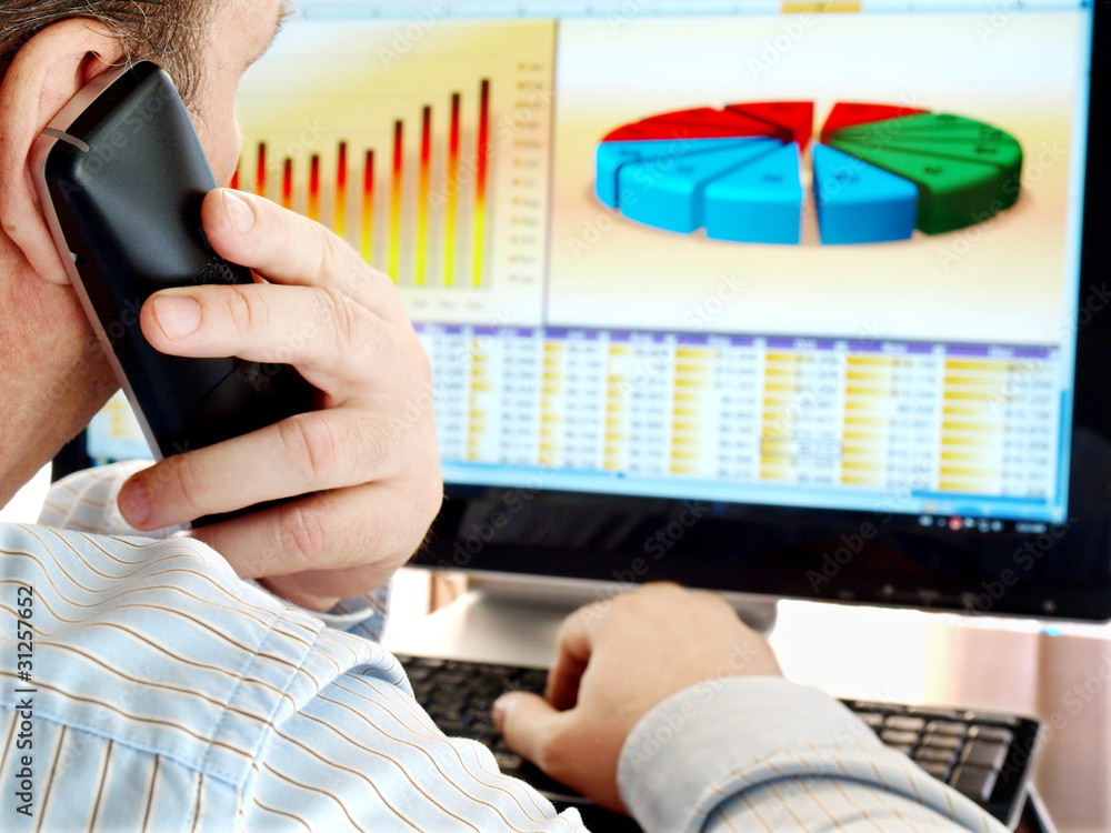Fototapete Man on a phone analyzing financial data and charts on computer