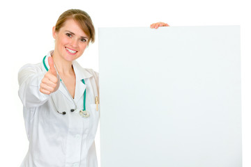 Female doctor holding blank billboard and showing thumbs up