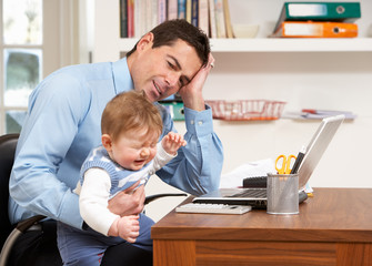 Stressed Man With Baby Working From Home Using Laptop