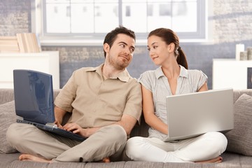 Young couple sitting on sofa using laptop smiling