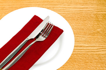 Knife and fork on red napkin on round white plate.