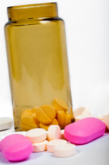 Medicine bottle with purple and yellow pills against white isola
