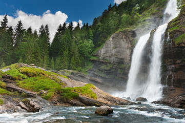 Alpine waterfall in mountain forest under blue sky. - 31325204