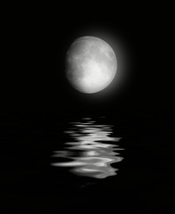 The full moon in the night sky reflected in water