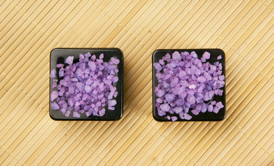 Two black bowls filled with purple salt on a bamboo mat
