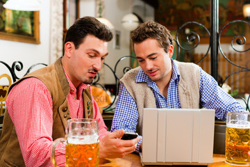 Zwei Freunde in bayerischer Wirtschaft mit Laptop